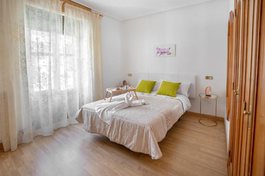 a white bedroom with a large bed with green pillows at Apartamento Candela in Salamanca