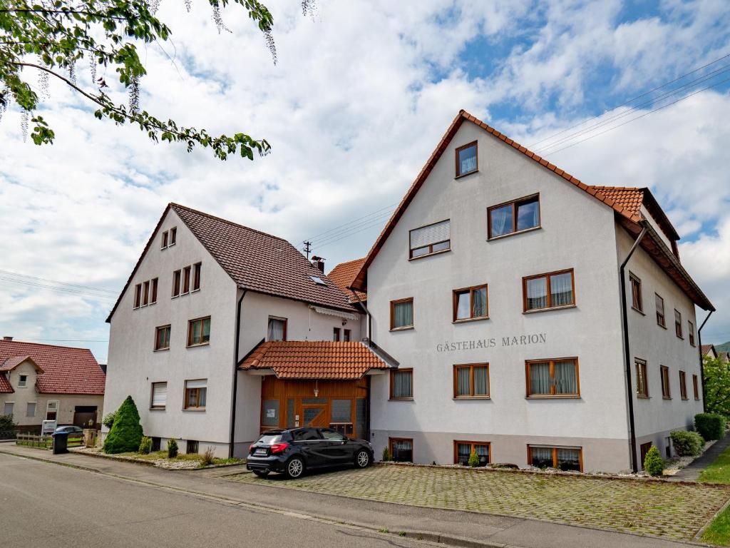 Un bâtiment blanc avec une voiture garée devant. dans l'établissement Gästehaus Marion, à Dettingen an der Erms