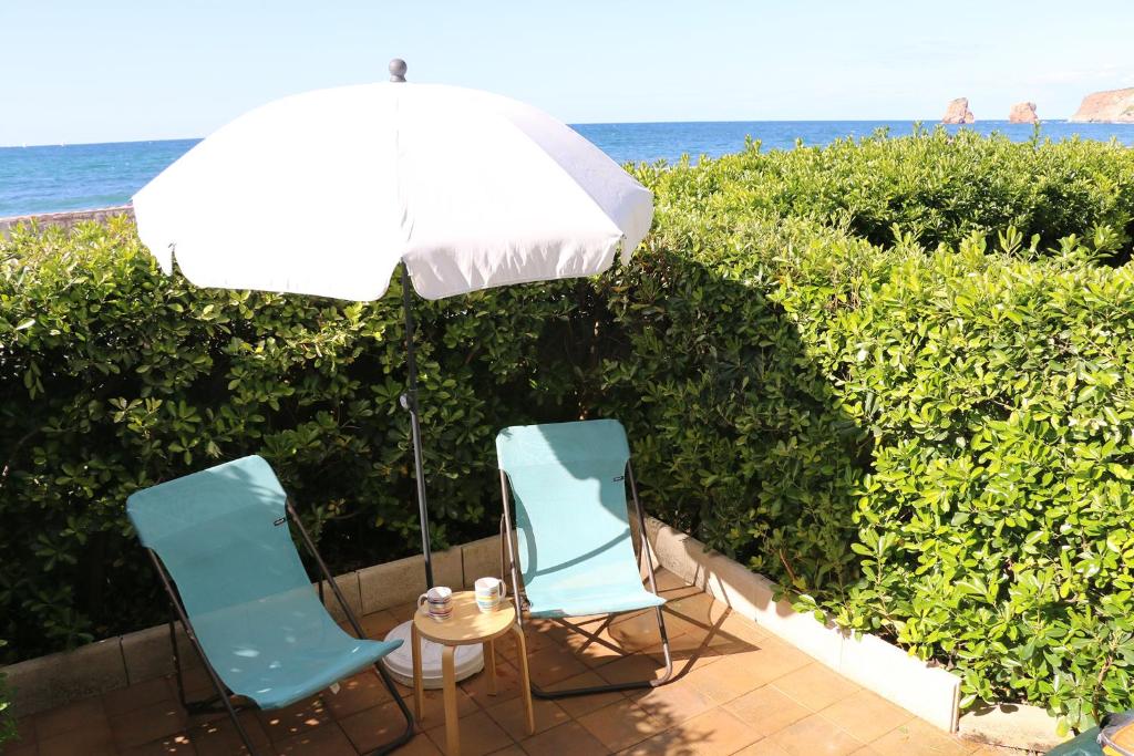 2 Stühle und ein Tisch mit Sonnenschirm in der Unterkunft Hendaye Beach Studio, front de mer avec parking privé in Hendaye