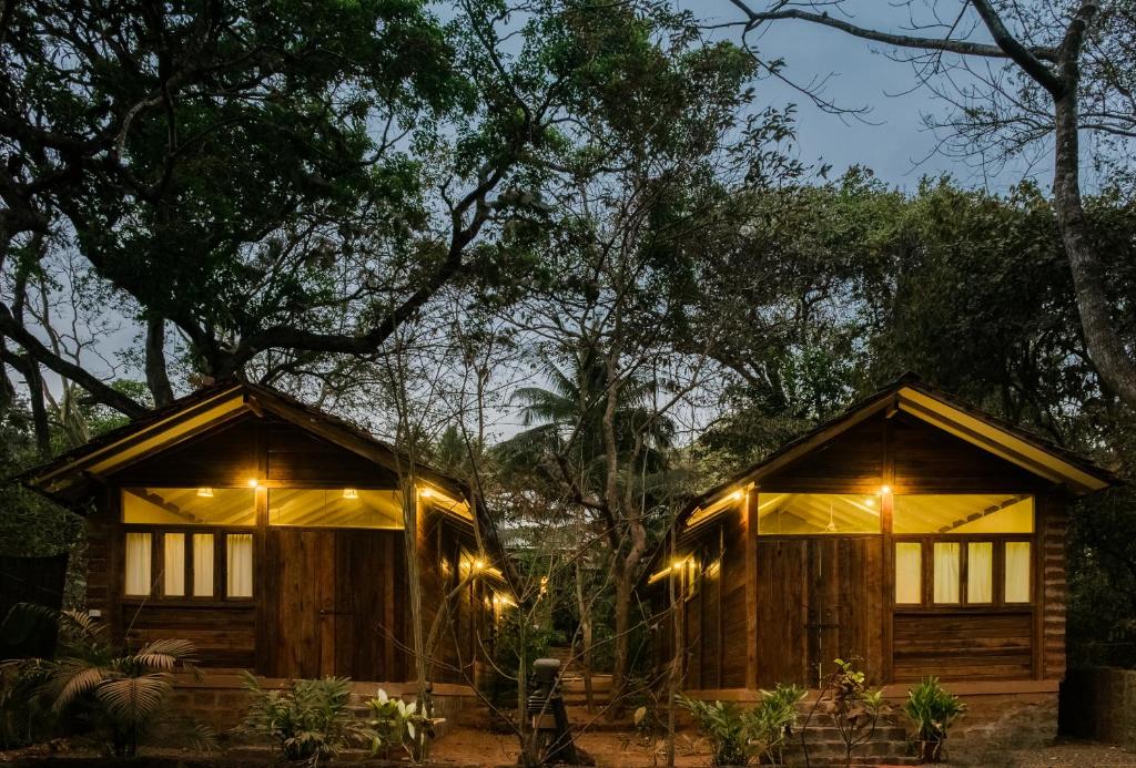 two wooden cabins with lights in the woods at night at Namaste Jungle - A Boutique Homestay in Assagao