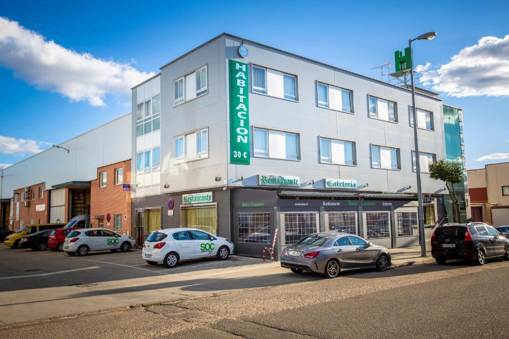 Un gran edificio con coches aparcados delante. en Hostal Campestre, en La Cistérniga