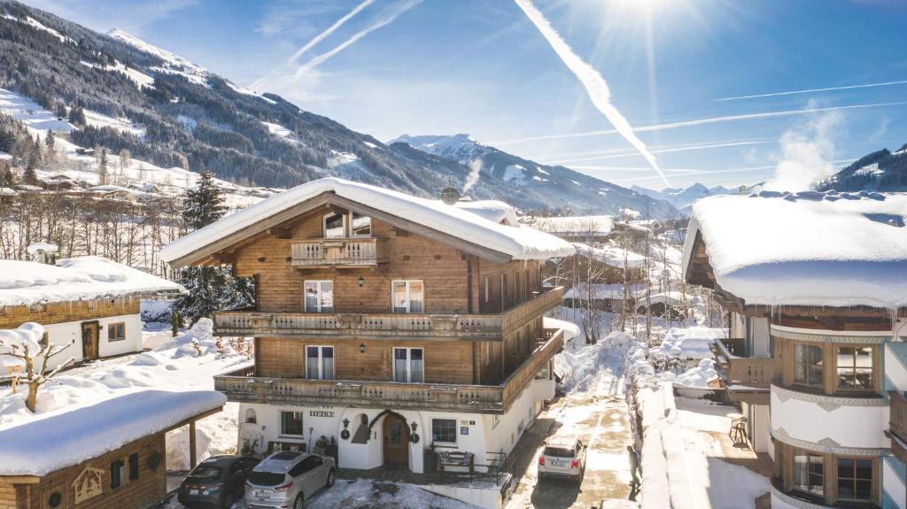 una casa in legno nella neve con montagne sullo sfondo di Hotel-Pension Heike a Kitzbühel
