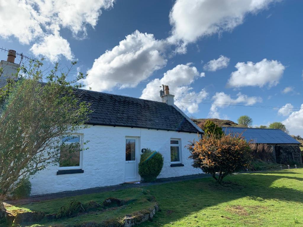 una casa de campo blanca en un césped con un cielo azul en Heatherland Cottage, en Portree
