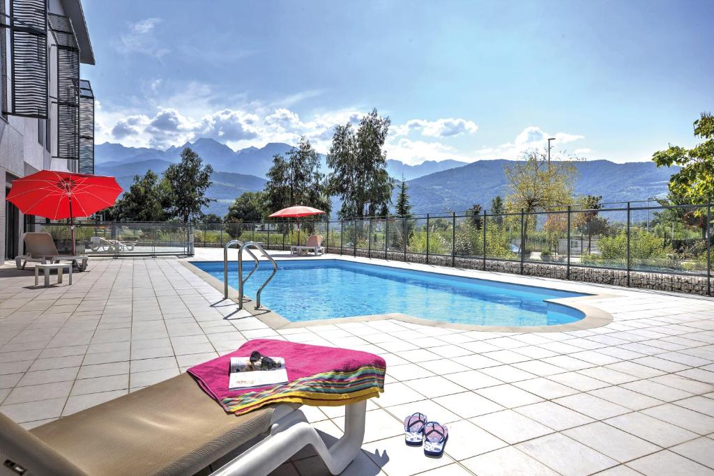 - une piscine avec une table et un parasol rouge dans l'établissement Appart'City Confort Grenoble Inovallée, à Montbonnot-Saint-Martin
