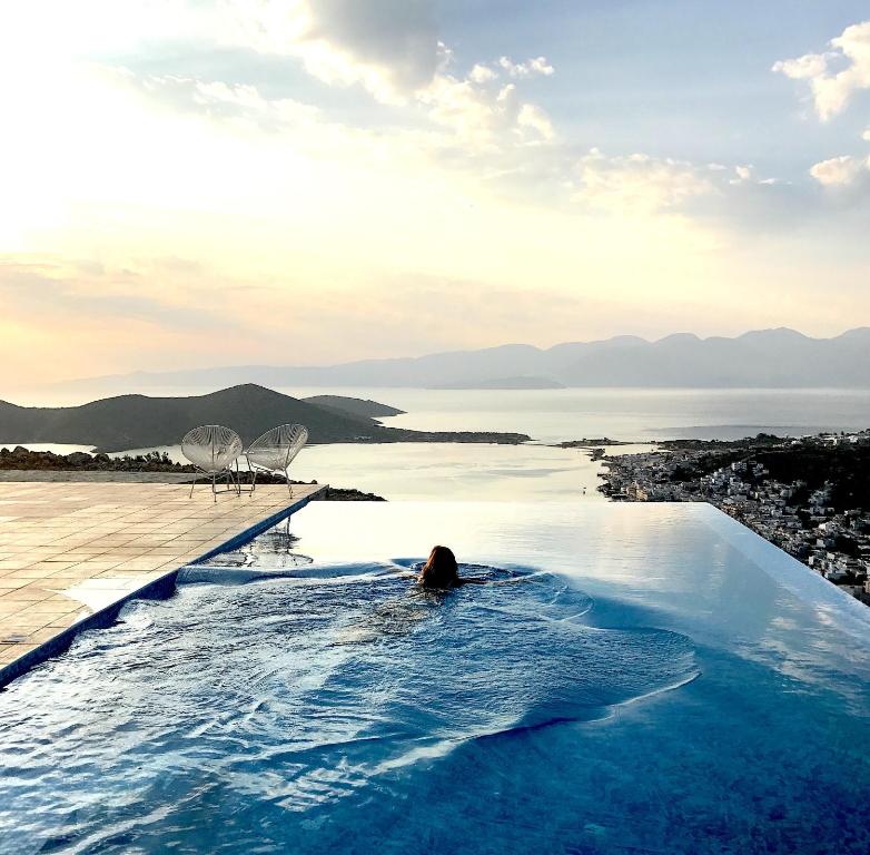 a person in a infinity pool overlooking a body of water at Villa Estée, luxury villa with private infinity pool and jacuzzi in Elounda