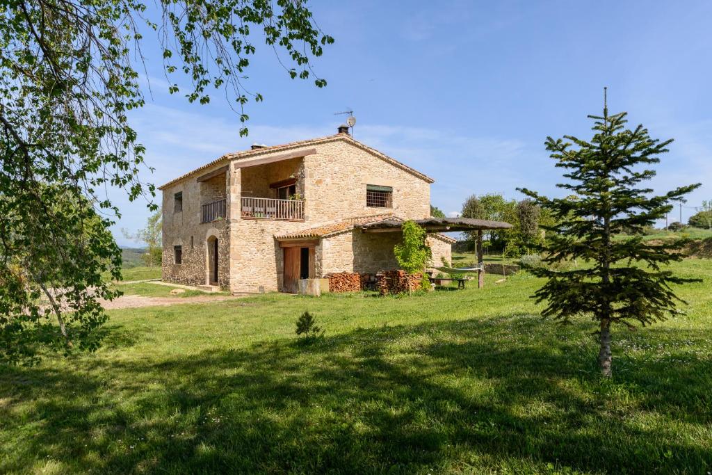 une ancienne maison en pierre dans un champ avec un arbre dans l'établissement Cal Menescal, à Les Olives