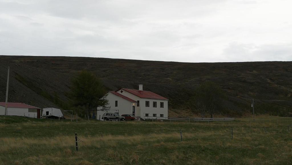 a white house in a field in front of a hill at Thorbrandsstadir Farm Holidays in Þorbrandsstaðir
