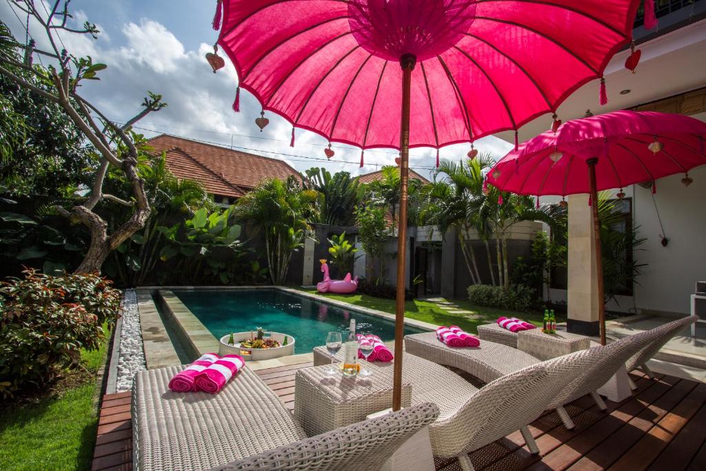 une terrasse avec un parasol et des chaises roses ainsi qu'une piscine dans l'établissement Villa Zakira, à Canggu