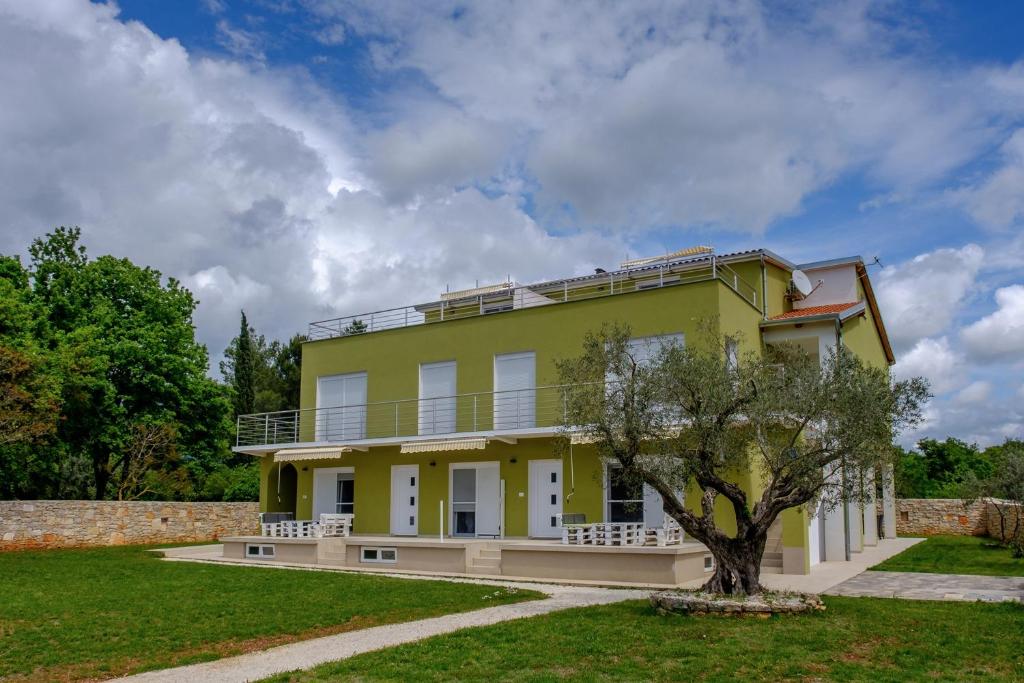 Una casa amarilla con un árbol delante. en Apartments Nogic, en Peroj