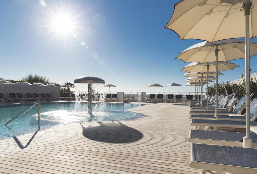 una piscina con sombrillas y sillas y una piscina en Hotel Cambridge en Lido di Jesolo