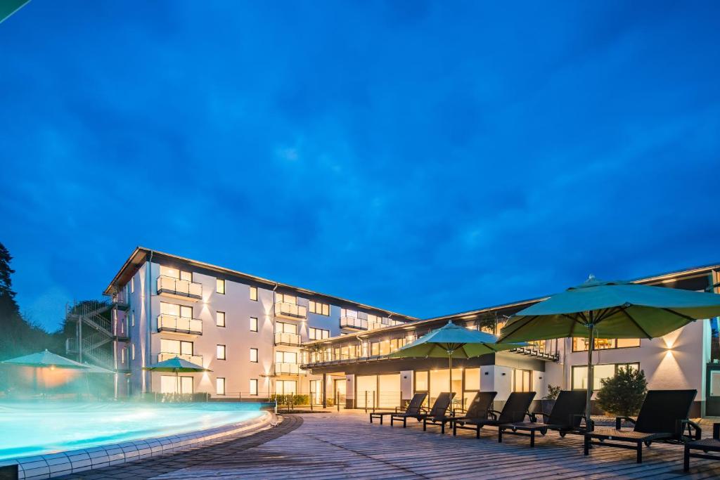 a hotel with chairs and umbrellas next to a swimming pool at Thermalhotel Aulendorf in Aulendorf