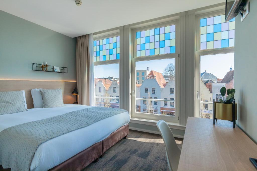 a bedroom with a bed and two large windows at City Hotel Rembrandt in Leiden