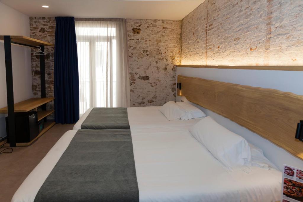 a bedroom with two beds and a brick wall at Hostal Paris in Barcelona