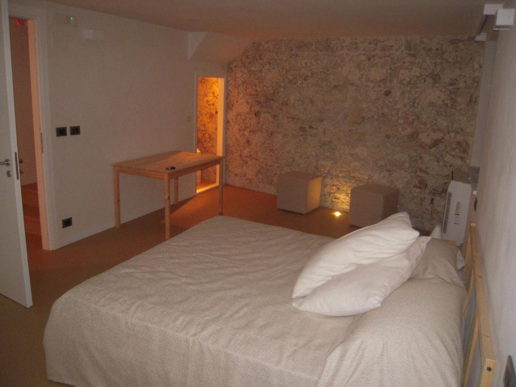 1 dormitorio con cama blanca y pared de piedra en Al Postale 17, en Erice