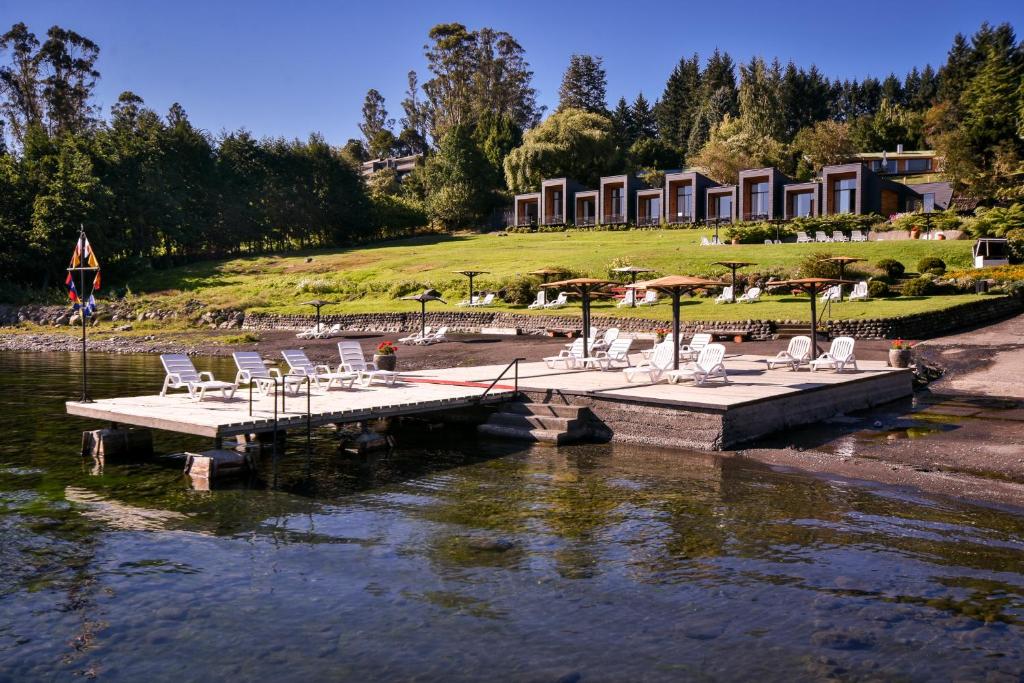 a dock with chairs and umbrellas on a body of water at Hotel y Cabañas El Parque in Villarrica