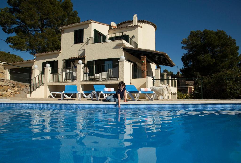 una mujer sentada en una piscina frente a una casa en Torre Orquidaceae - Plus Costa Brava, en L'Estartit