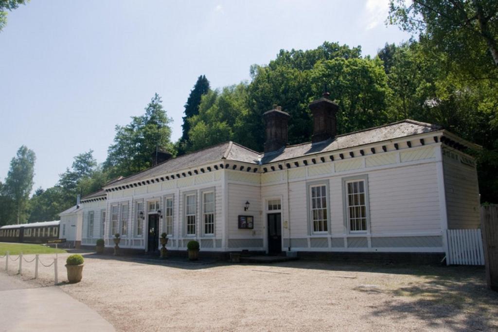 an old white building with trees in the background at The Old Railway Station in Petworth