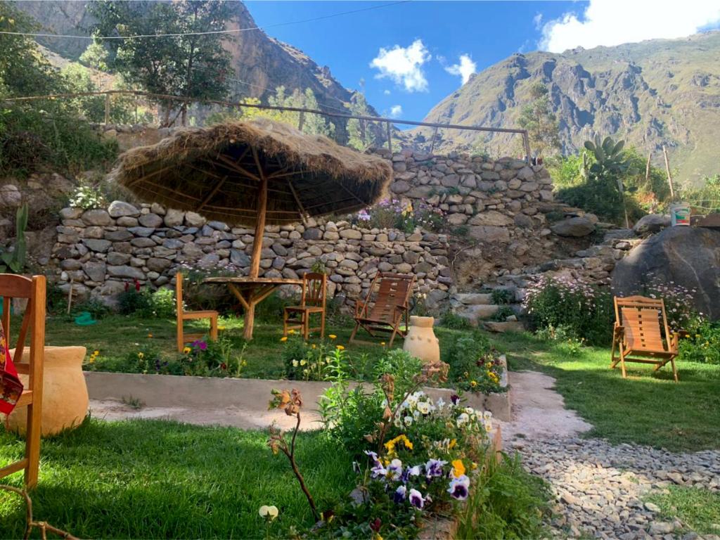 a garden with chairs and an umbrella and a stone wall at Inka Khawarina Tambo Lodge in Ollantaytambo