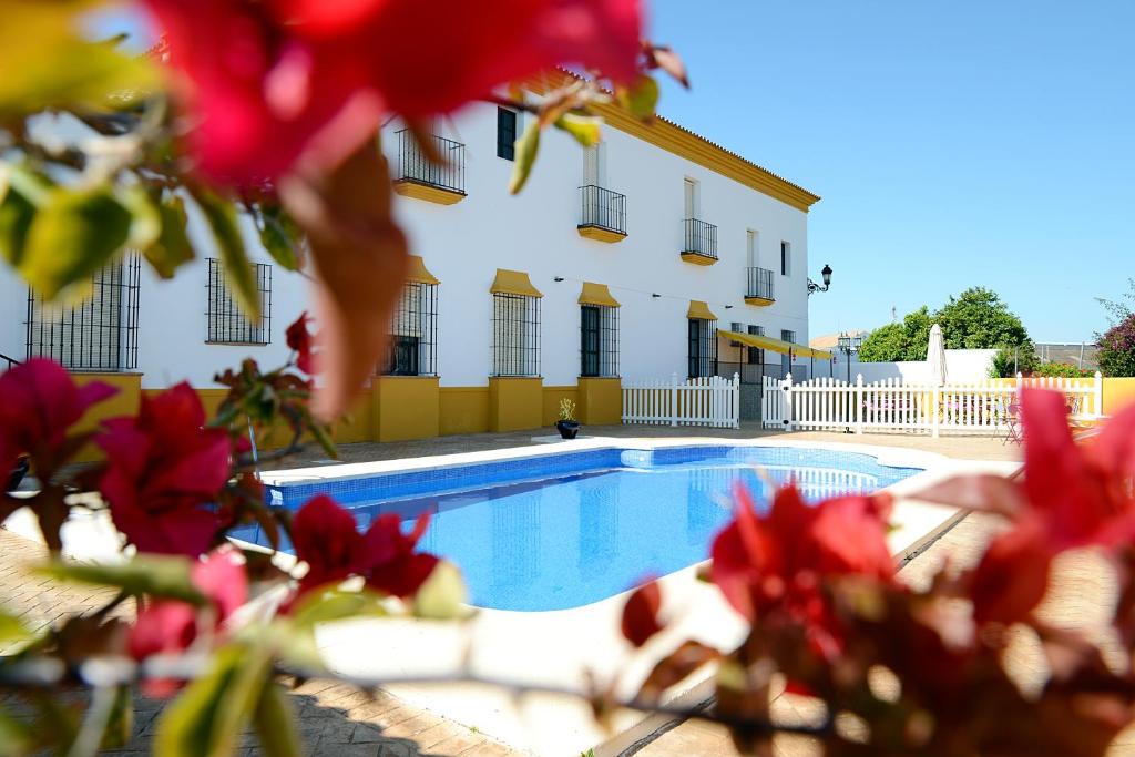 a swimming pool in front of a building with red flowers at Hotel Andalou in Montellano