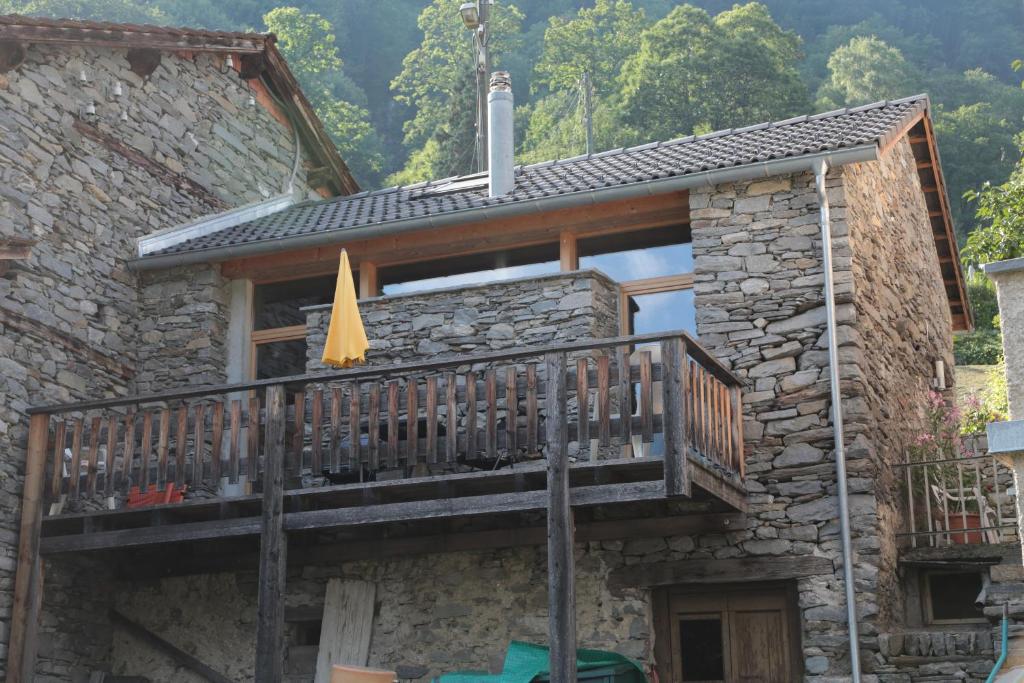 een stenen huis met een balkon met een parasol bij Rustico in Verdabbio