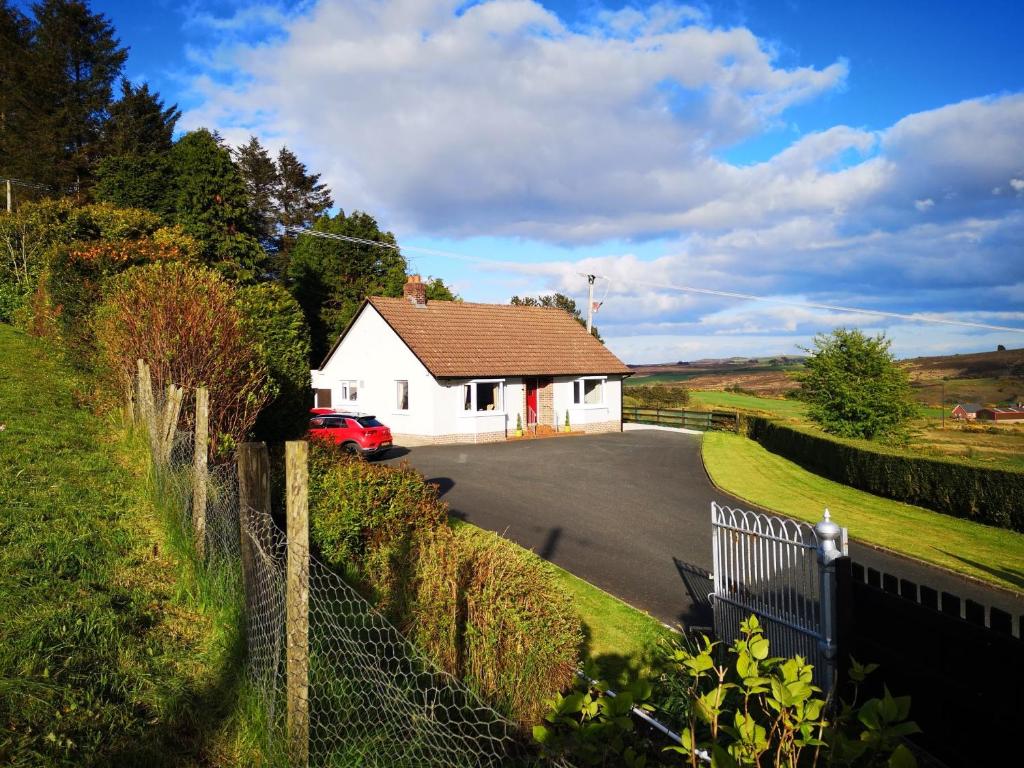 een wit huis met een rode auto op een weg bij Alice's Cottage in Omagh