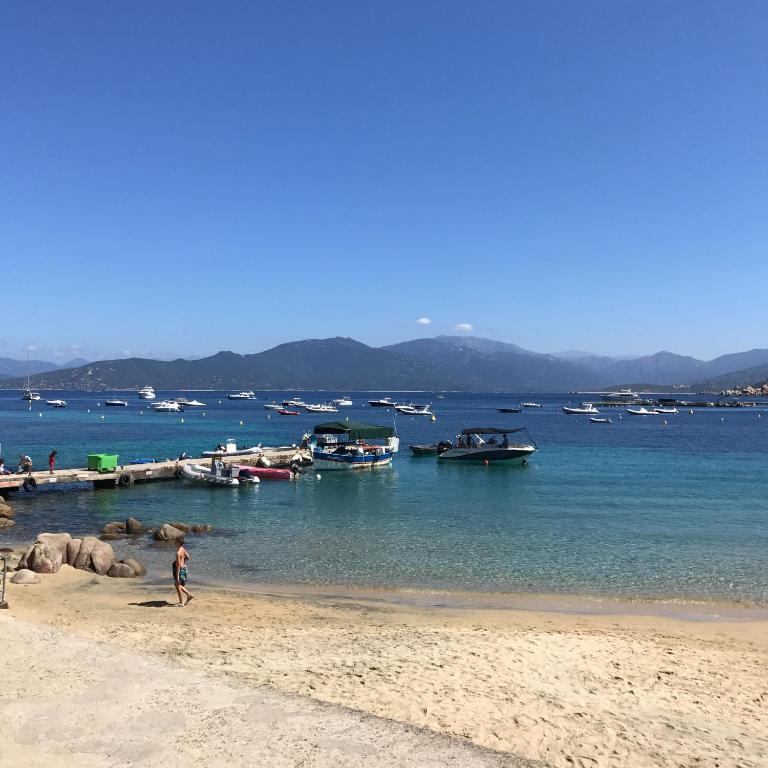 a person walking on a beach with boats in the water at HOTEL CAMPOMORO in Belvédère-Campomoro