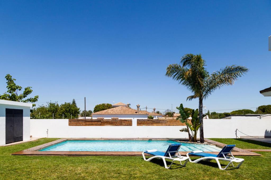 a swimming pool with two chairs and a palm tree at Villa La Barrosa in Chiclana de la Frontera