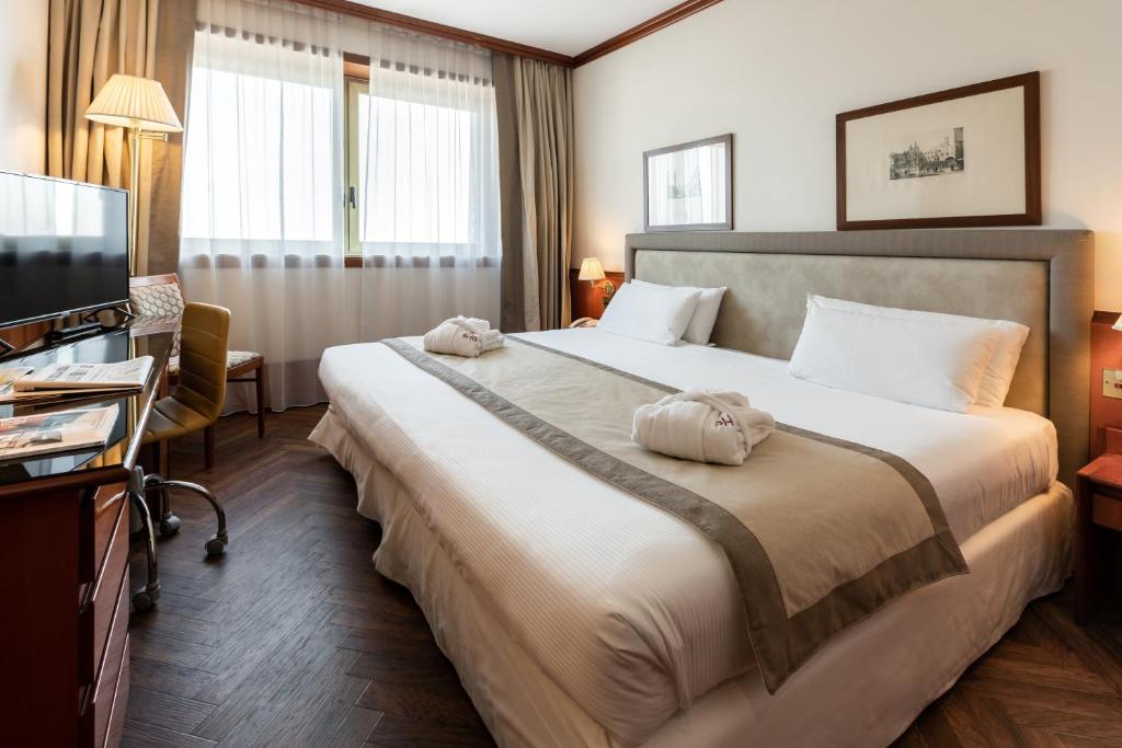 サン・マルティーノ・ブオン・アルベルゴにあるHotel Catulloの大型ベッドとテレビが備わるホテルルームです。