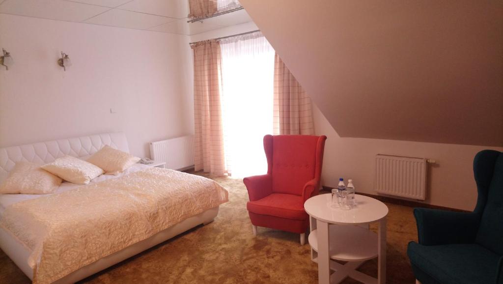 a bedroom with a bed and a red chair and a table at Hotel Milord in Pułtusk