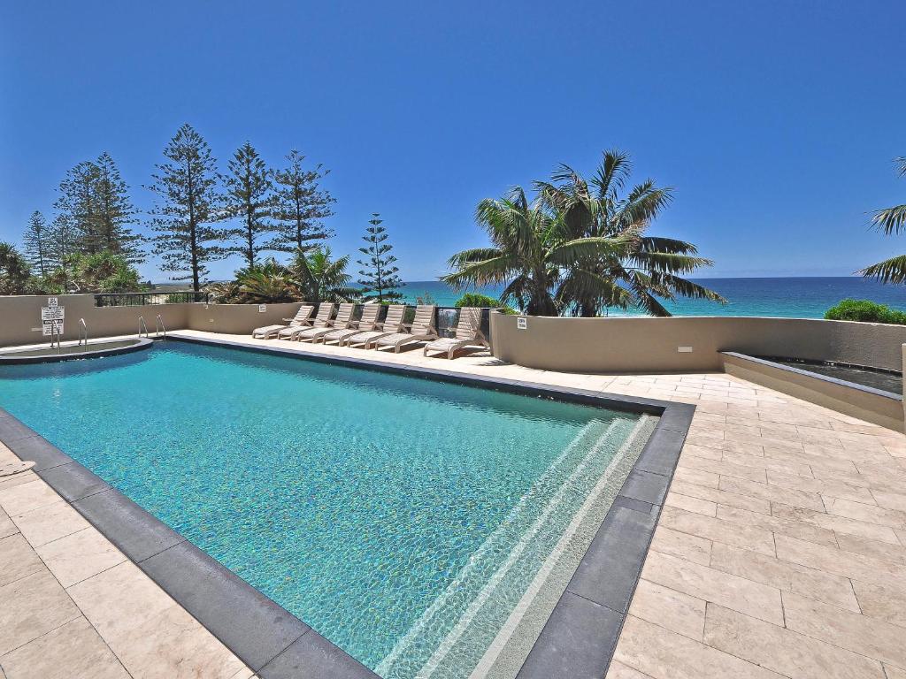 a swimming pool with chairs and the ocean in the background at Clubb Coolum Beach Resort in Coolum Beach