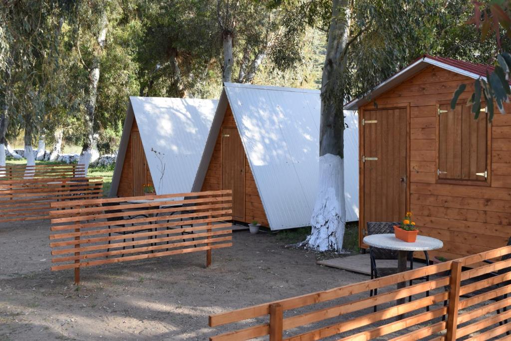 a group of small wooden shelters with a table and trees at Camping Kea in Pisses