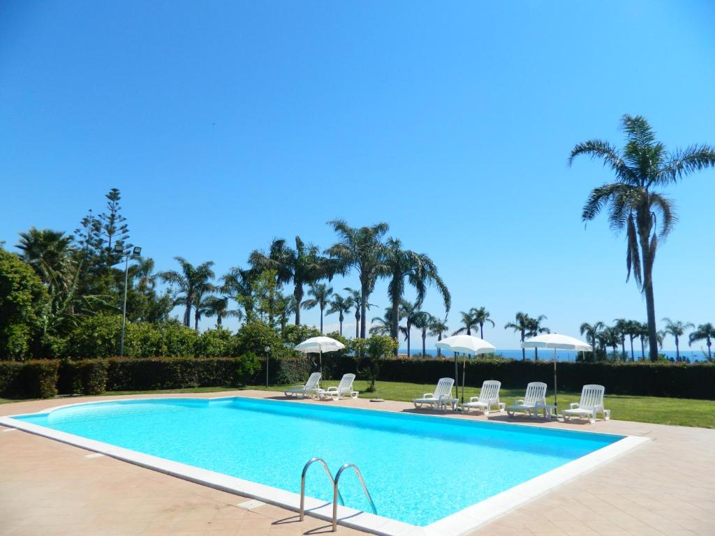 a swimming pool with chairs and palm trees at Agriturismo La Grevillea in Riposto