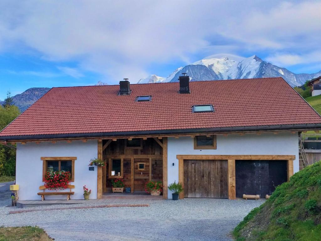 a house with a red roof with mountains in the background at La grange d'Aldaré Chambres d'hôtes in Combloux