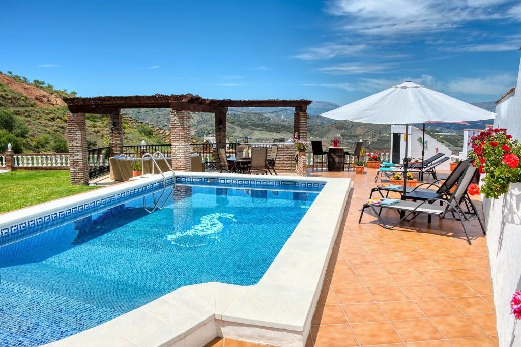 uma piscina com mesa e cadeiras e um guarda-sol em Casa las Torres B&B em Iznate