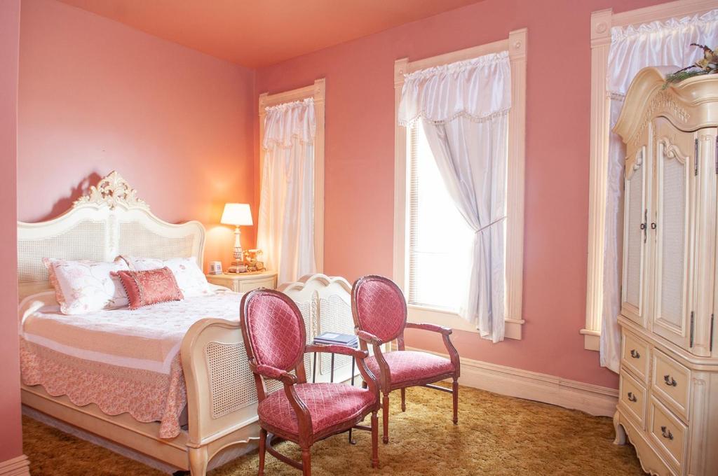 um quarto com paredes cor-de-rosa e uma cama com 2 cadeiras em The Historic Wolf Hotel em Ellinwood