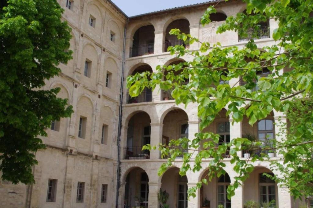 un vieux bâtiment avec des fenêtres cintrées et un arbre dans l'établissement Clos des Arts Suspendus, à Avignon