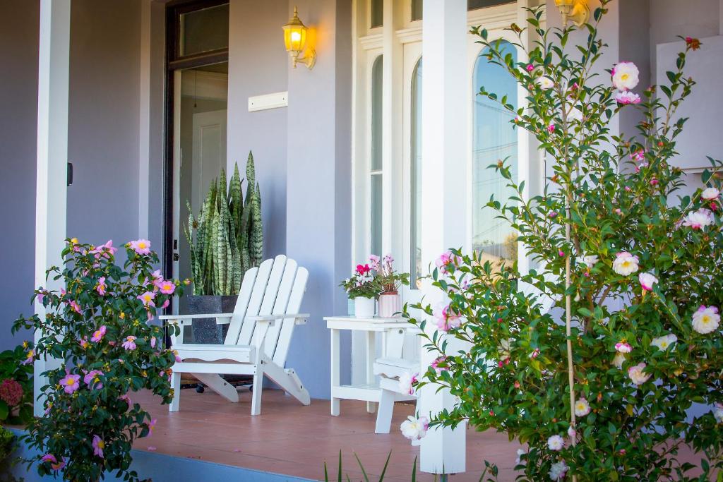 a porch with flowers and a white chair at Camellia Cottage in Cessnock