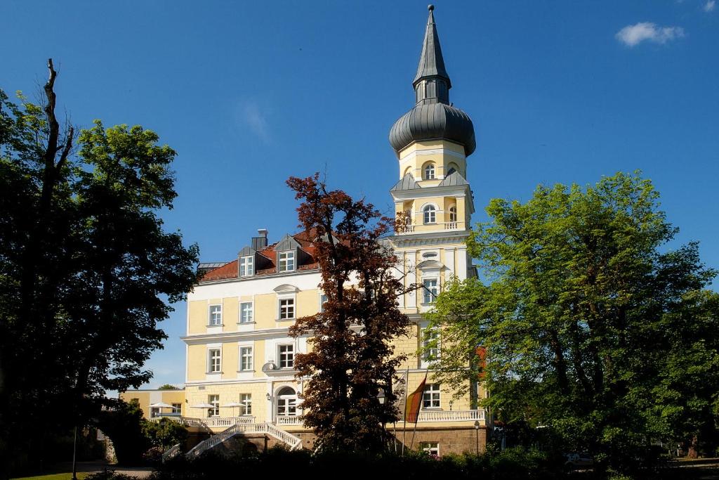 ein hohes weißes Gebäude mit einem Uhrturm in der Unterkunft Hotel Schloss Schwarzenfeld in Schwarzenfeld