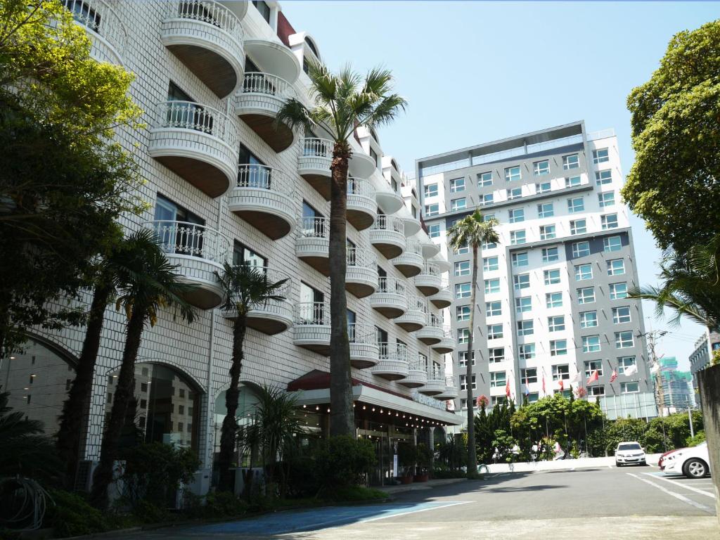 um edifício alto e branco com palmeiras em frente em Pearl Hotel Jeju em Jeju