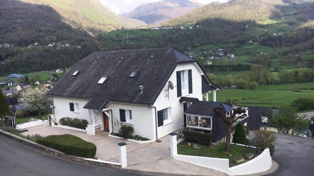 une maison blanche avec un toit noir et des montagnes en arrière-plan dans l'établissement MAISON BELLEVUE 3 étoiles 4 à 10P, à Laruns