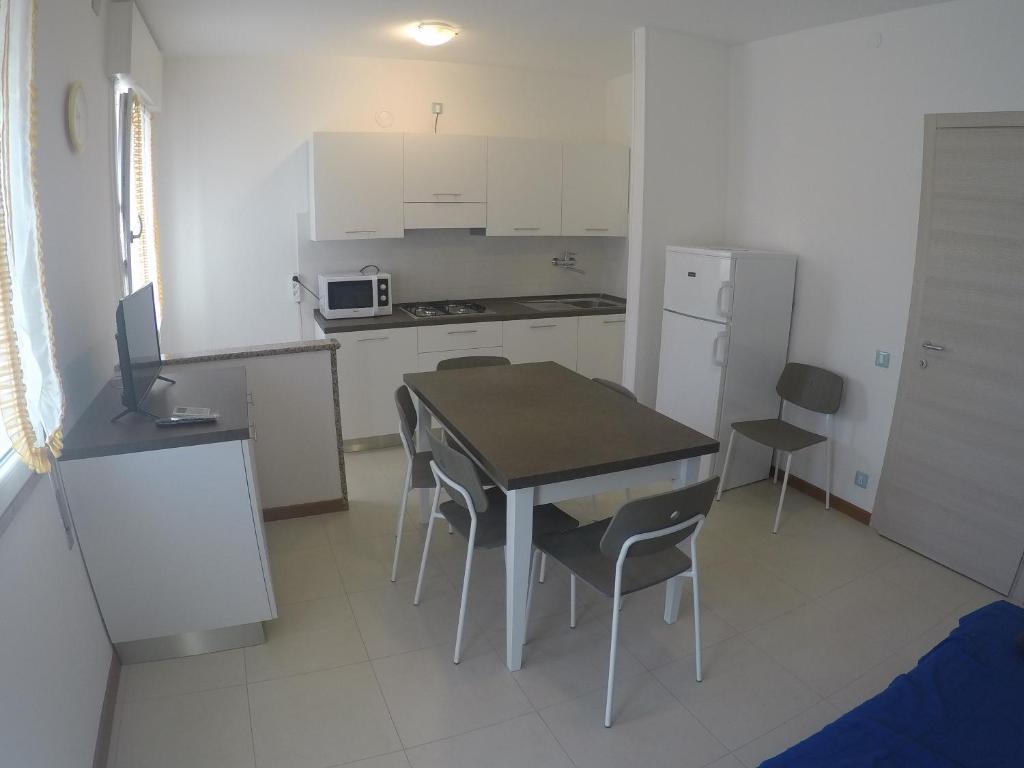 una cocina con mesa y sillas y una cocina con armarios blancos. en Appartamento Tintoretto - Agenzia Cocal, en Caorle