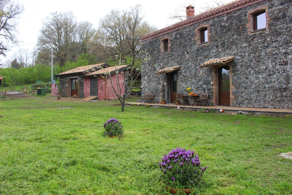 a stone house with purple flowers in the yard at Agriturismo La Caraffara sull' Etna in Puntalazzo