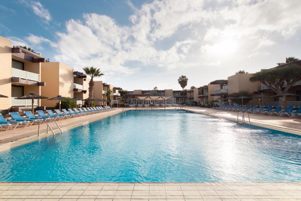 una gran piscina con sillas azules y edificios en Hotel Palia Don Pedro en Costa del Silencio