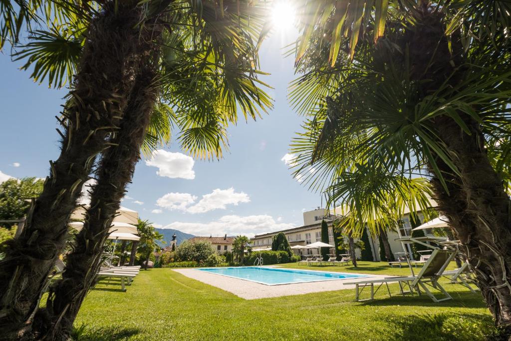 a swimming pool between two palm trees at Hotel Mandelhof ***S in Appiano sulla Strada del Vino