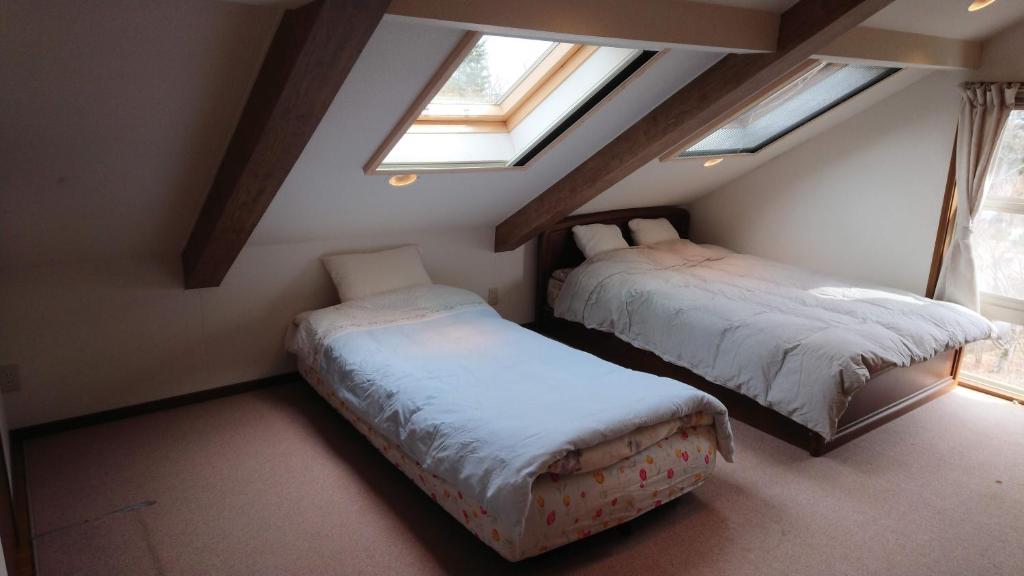 a attic room with two beds and two windows at Guest House 合歓木（ねむ） in Hokuto