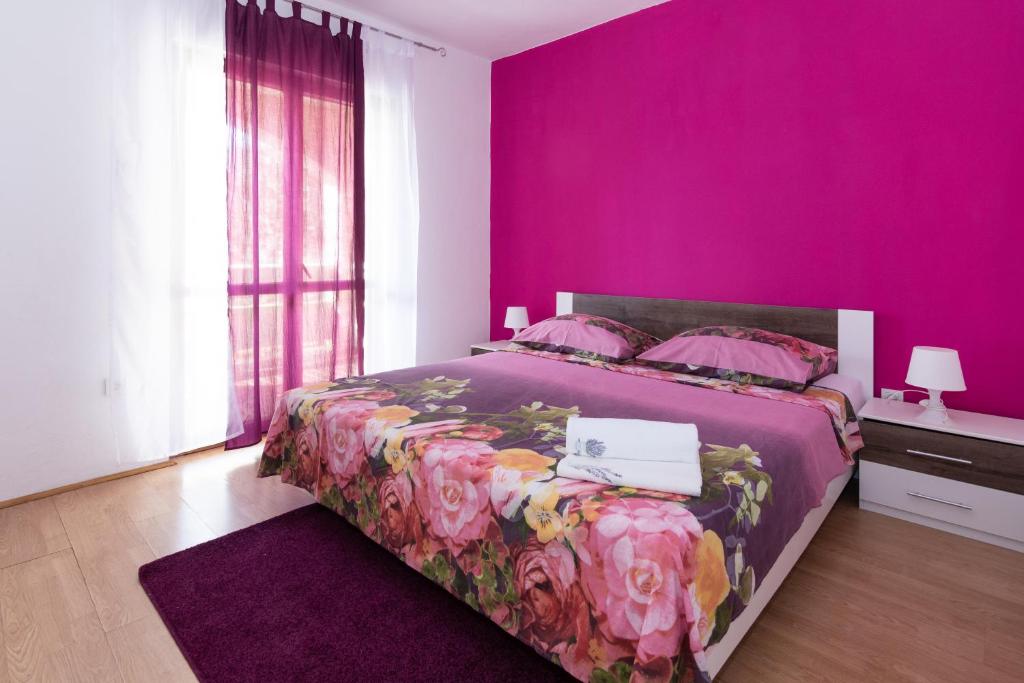 a pink bedroom with a bed with a purple wall at Apartments Luka in Pag