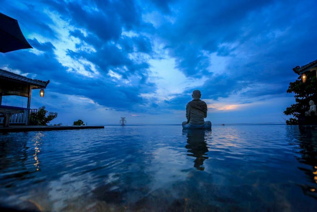 Un uomo seduto sull'acqua che osserva il tramonto di The Kayu Manis Villa a Lovina