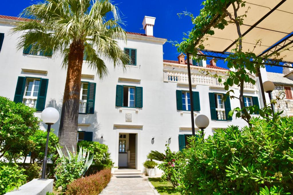 uma casa branca com persianas verdes e uma palmeira em Villa Giardino Heritage Boutique Hotel Bol em Bol