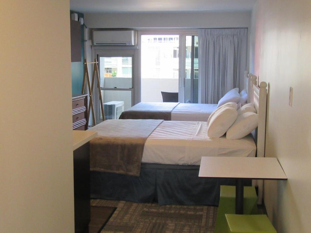 a bedroom with two beds and a table in a room at Waikiki Central Hotel - No Resort Fees in Honolulu