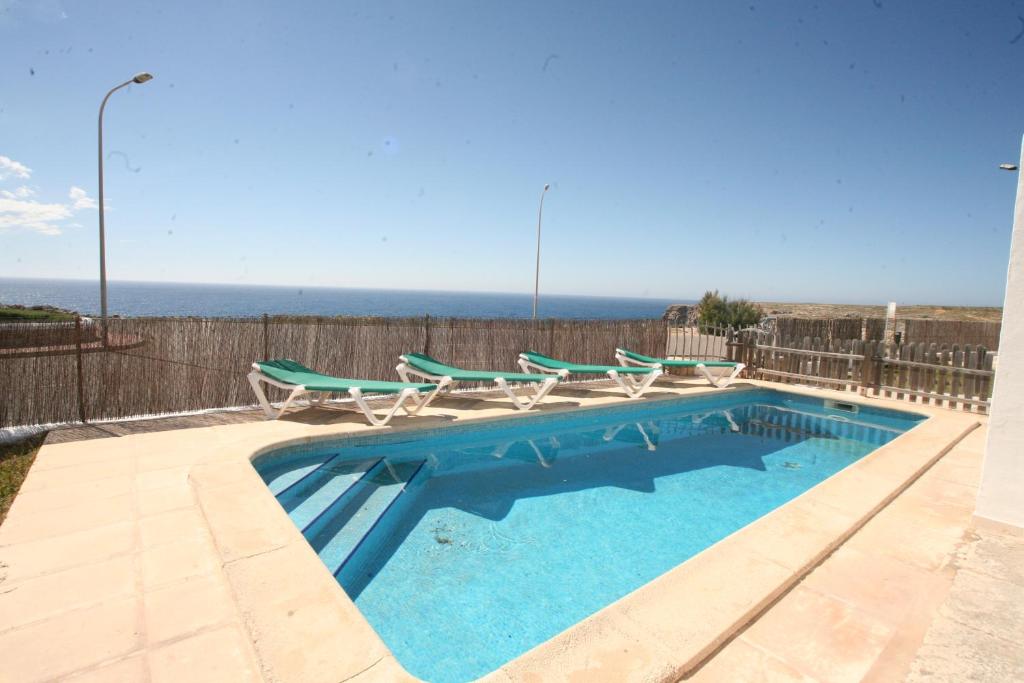 a swimming pool with chairs and the ocean in the background at Villa Victor - Primera linea mar, vista a puesta de sol in Cala en Blanes